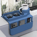 A blue silicone sofa armrest tray with a white mug, sunglasses, and side pockets holding a phone and remote.