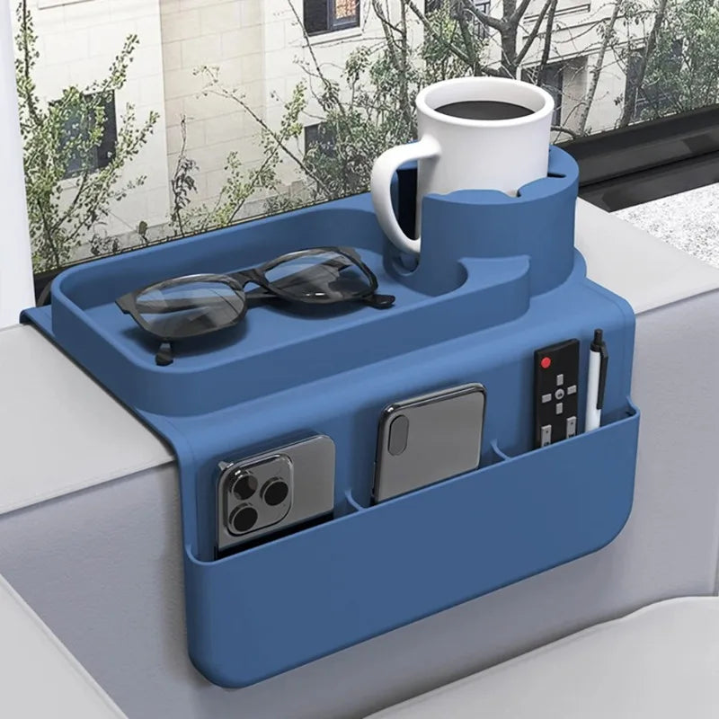 A blue silicone sofa armrest tray with a white mug, sunglasses, and side pockets holding a phone and remote.